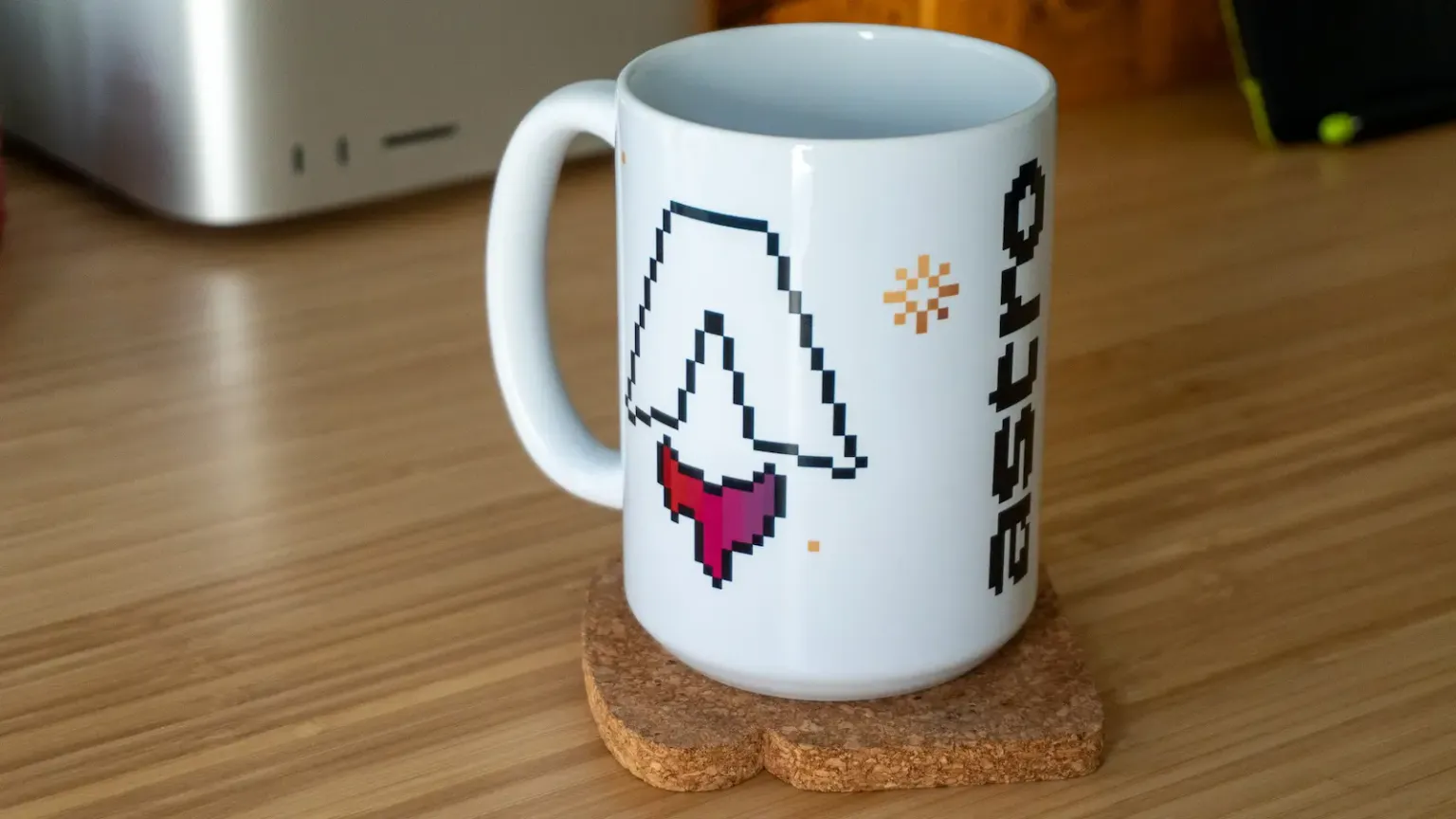 A white mug on a desk featuring a pixel art Astro logo.